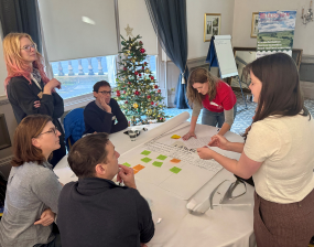 A group sit around a table discussing an A3 piece of paper with pink and green post-its on