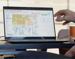 A hand hovering over a laptop showing a complex modelling system
