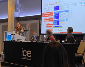 Vicky doing a presentation from behind a table on a stage, 3 other people are also sat behind the table